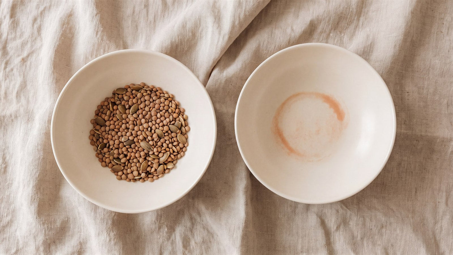 A ceramic bowl of dried lentils and pumpkin seeds beside an empty bowl marked with a faint terracotta ring