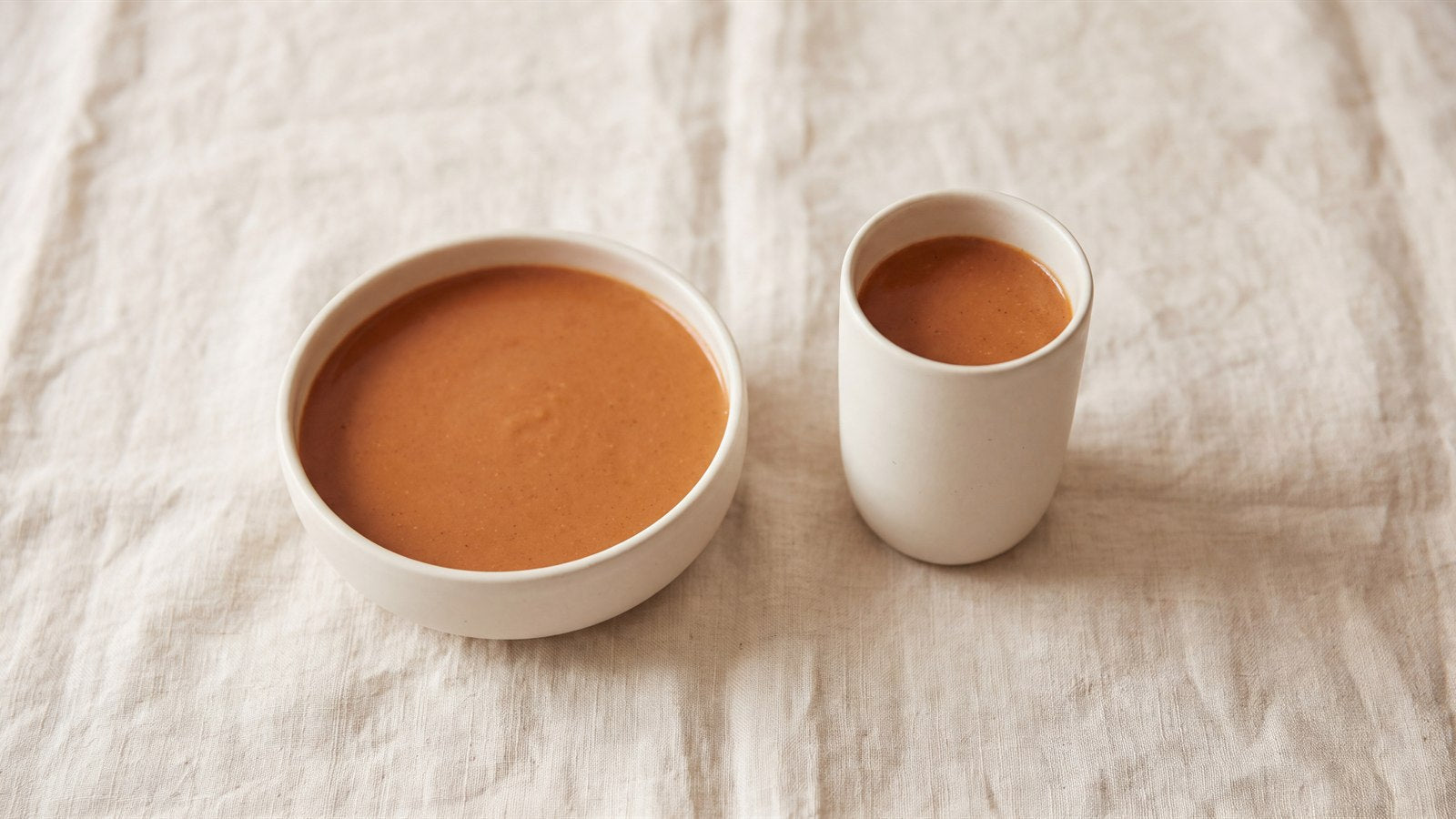 A wide shallow bowl and a tall narrow cup holding the same terracotta liquid at the same depth