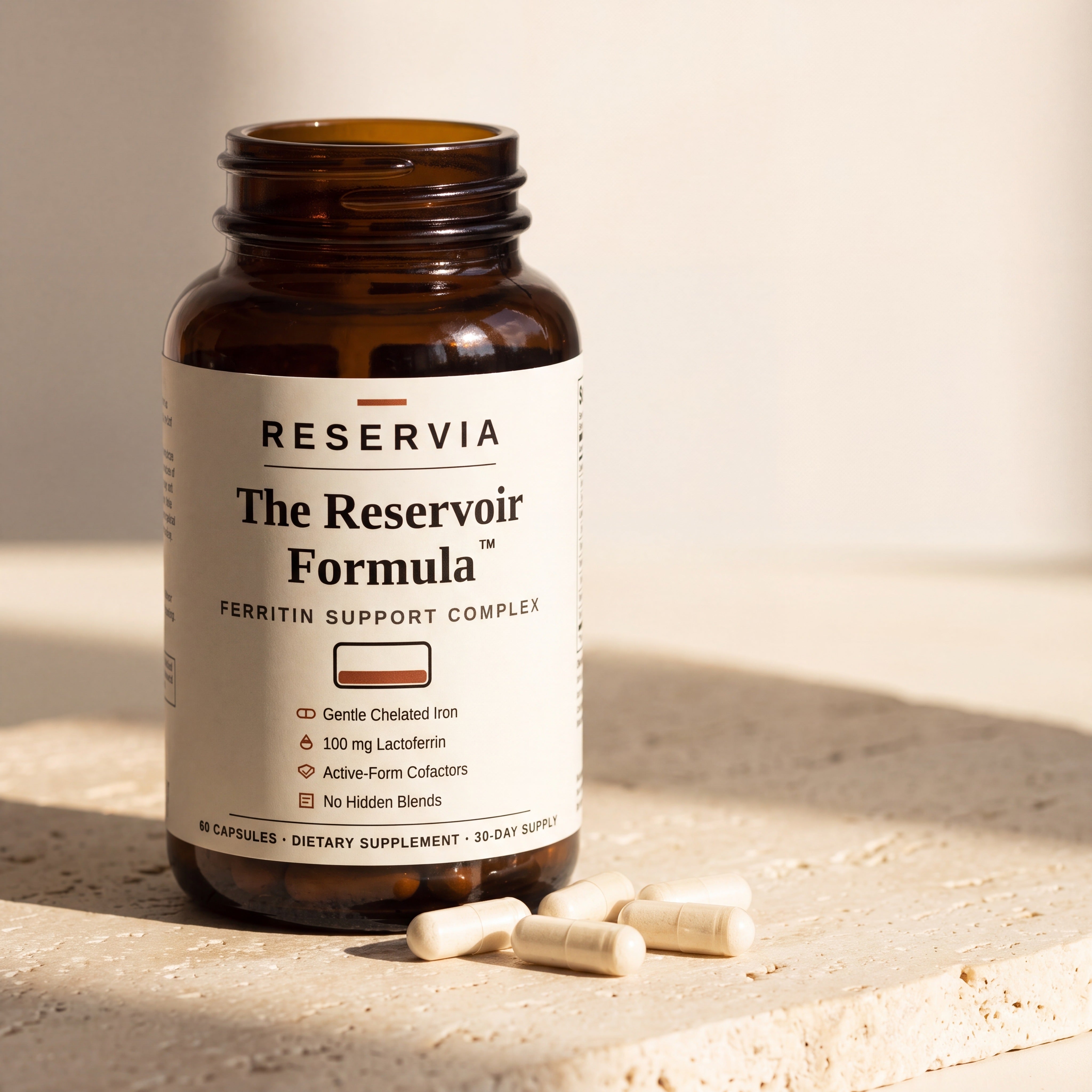 The Reservoir Formula bottle on a travertine slab in daylight, with loose ivory capsules beside it.