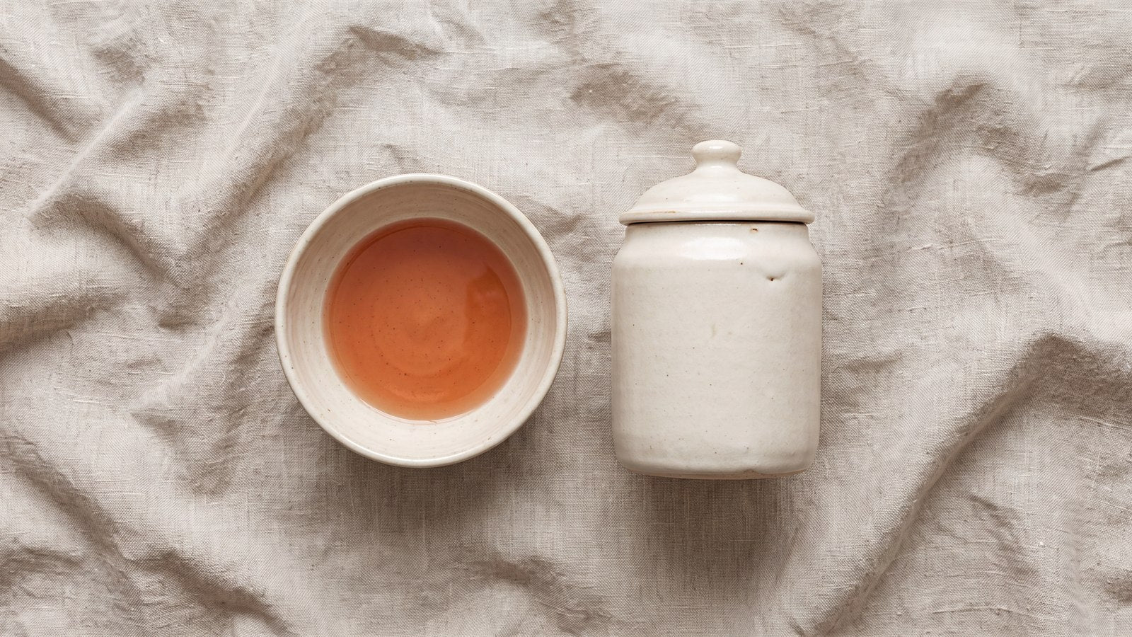 An open ceramic bowl holding terracotta liquid beside a sealed ceramic jar: iron in circulation and iron in storage