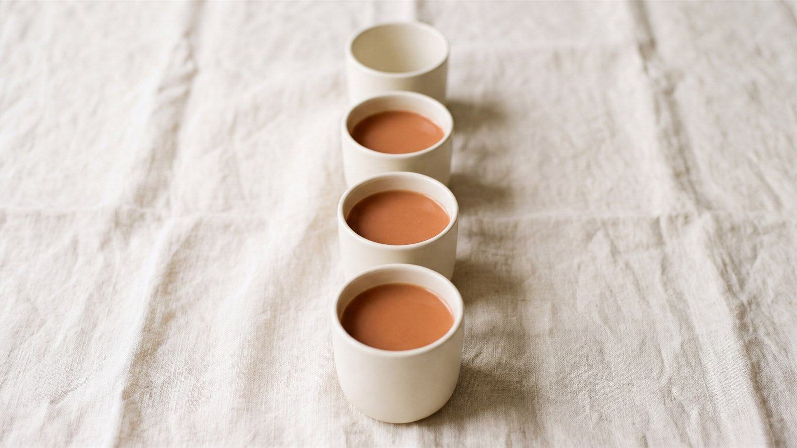 Four ceramic cups holding terracotta liquid and a fifth left empty at the back of the row
